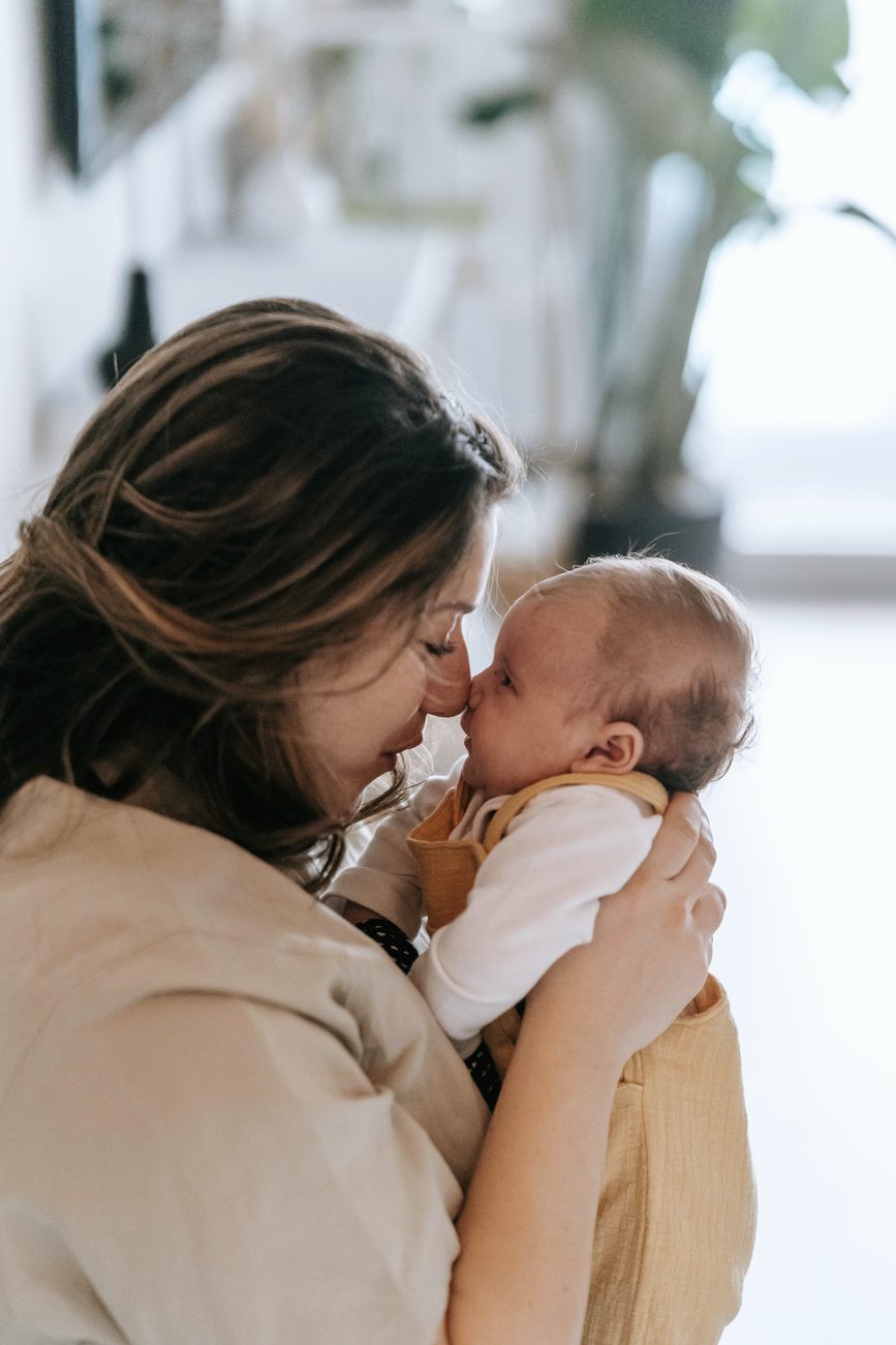 A mother touching noses with her baby by a window