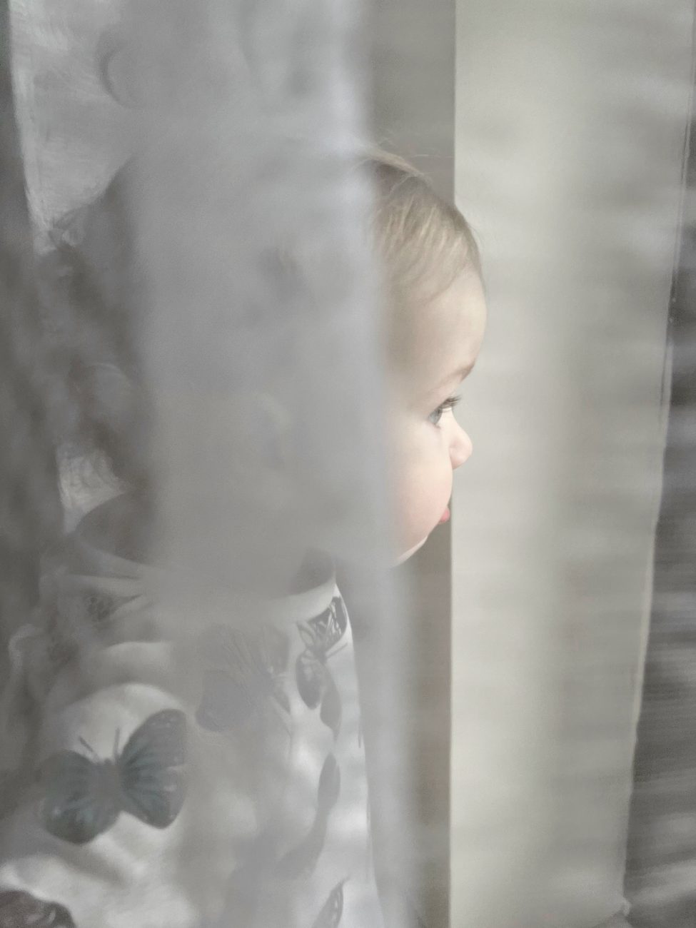 A baby peeking out from behind a sheer curtain